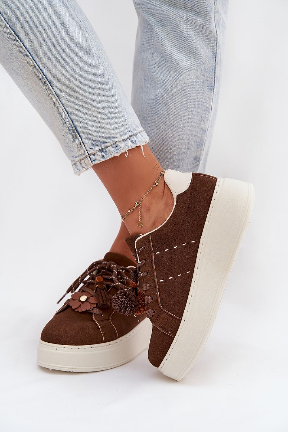 Brown platform sneakers with white soles worn with light blue jeans on a white background