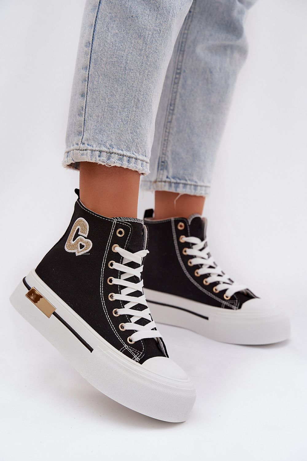 Black high-top sneakers with white laces worn with light blue jeans on a white background