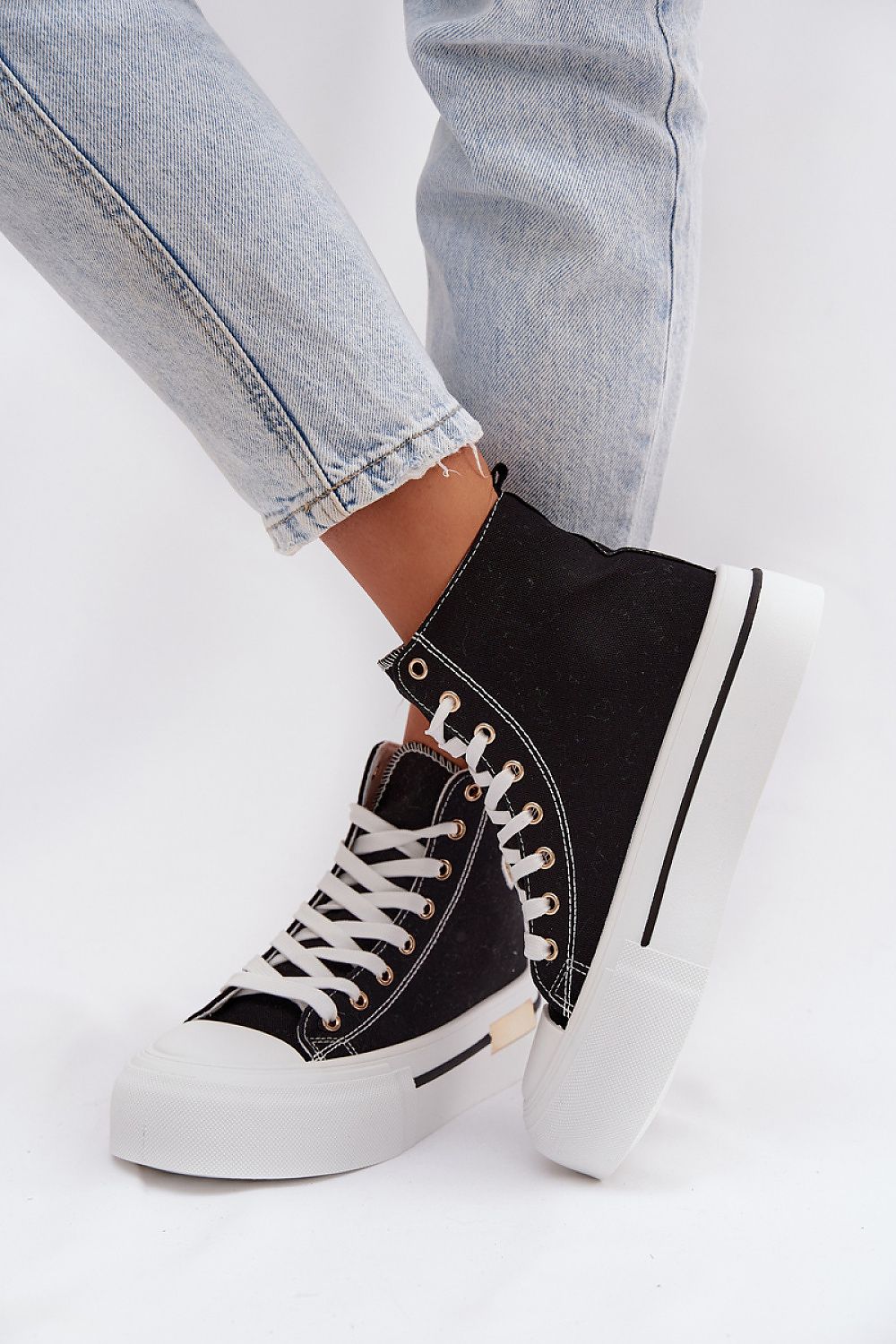 Black high-top sneakers with white soles worn with light blue jeans on a white background