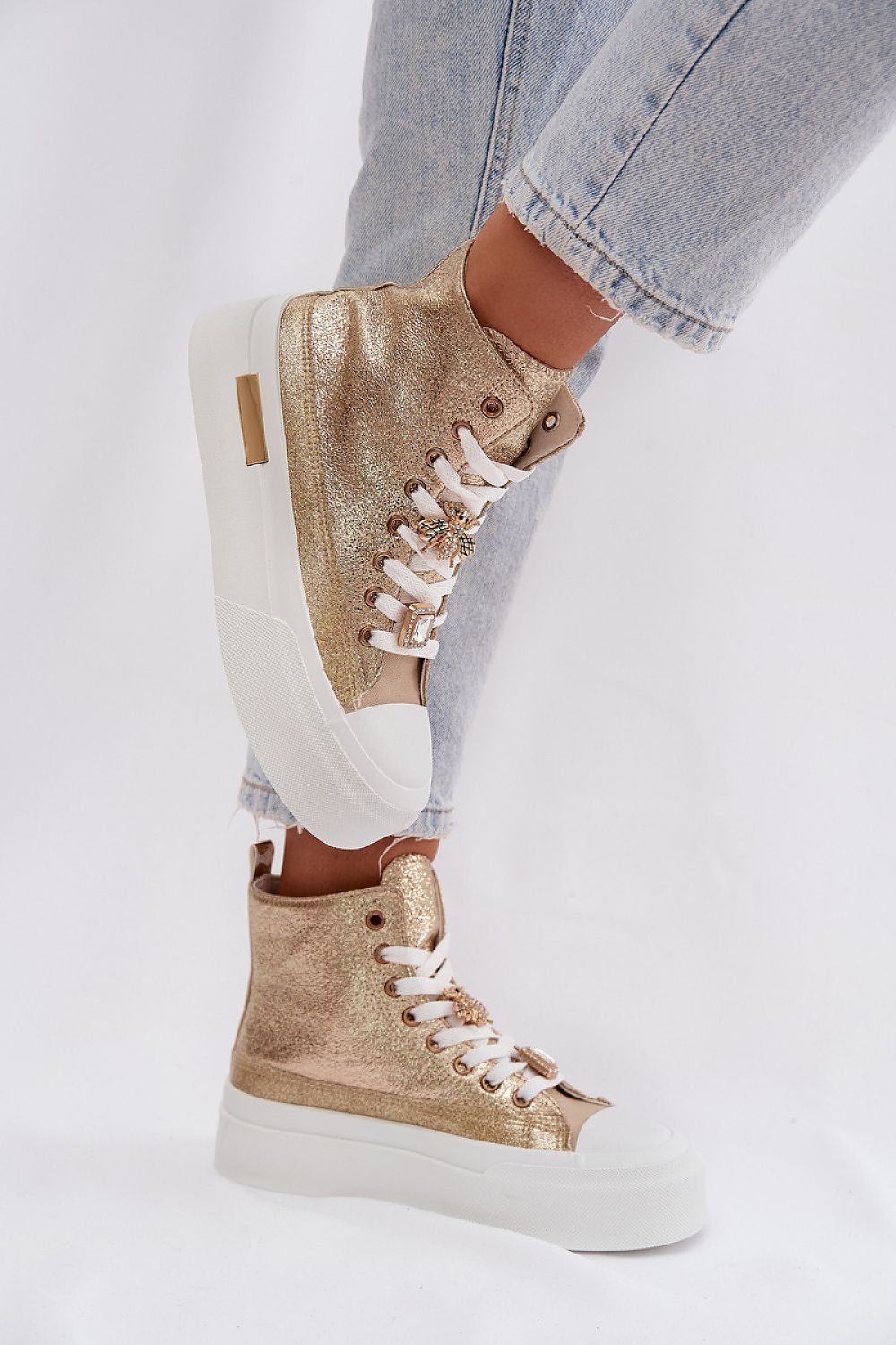 Gold high-top sneakers worn with light blue jeans on a white background