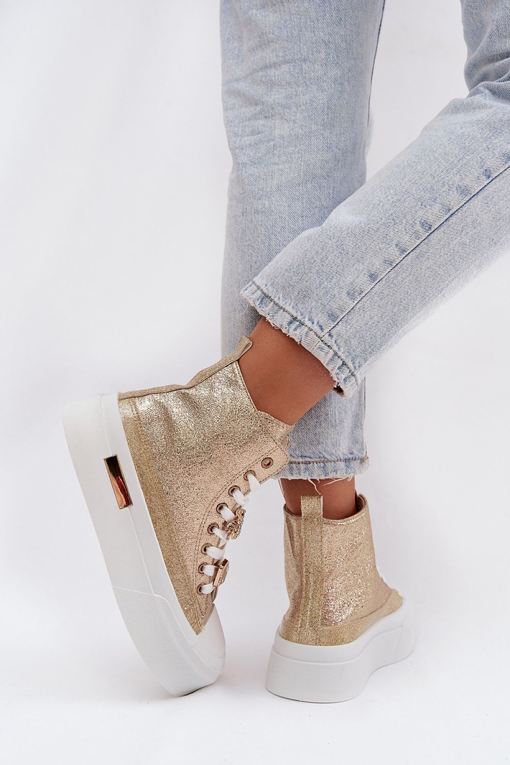 Gold glitter high-top sneakers with white soles worn with light blue jeans on a white background