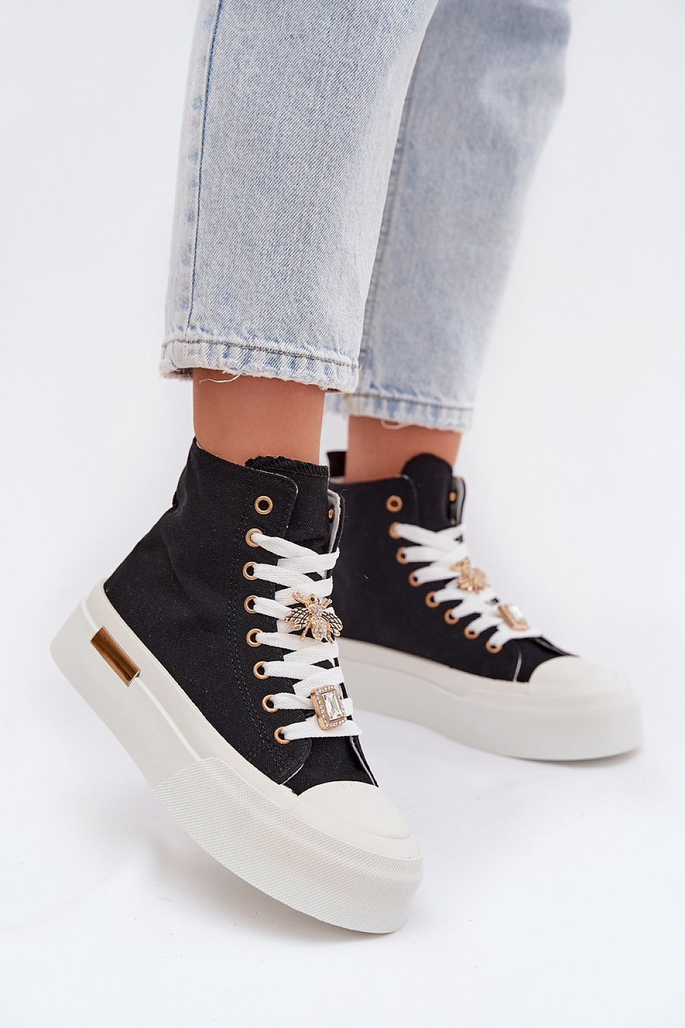 Black high-top sneakers with white soles worn with light blue jeans on a white background