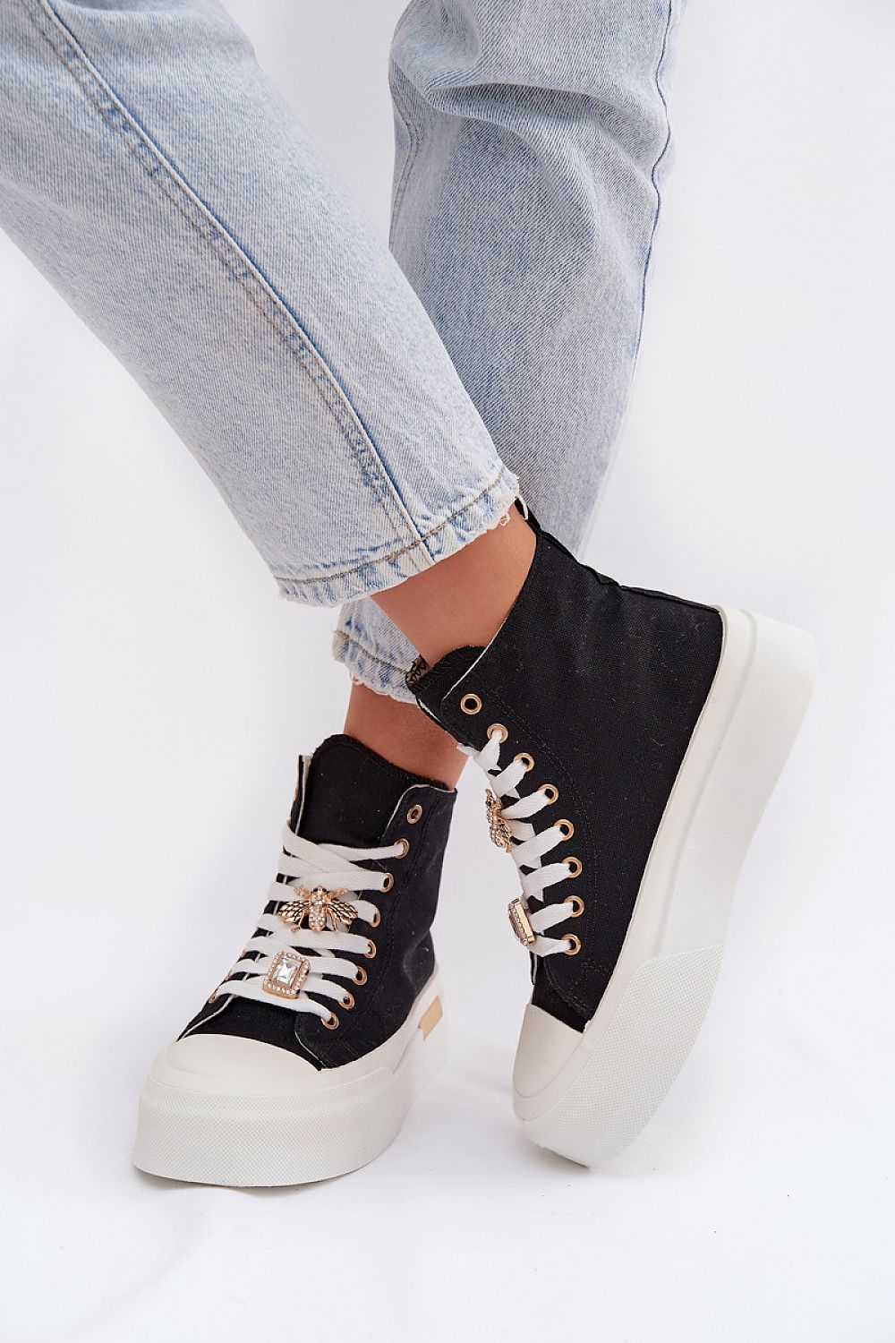 Black high-top sneakers with white laces worn with light blue jeans on a white background