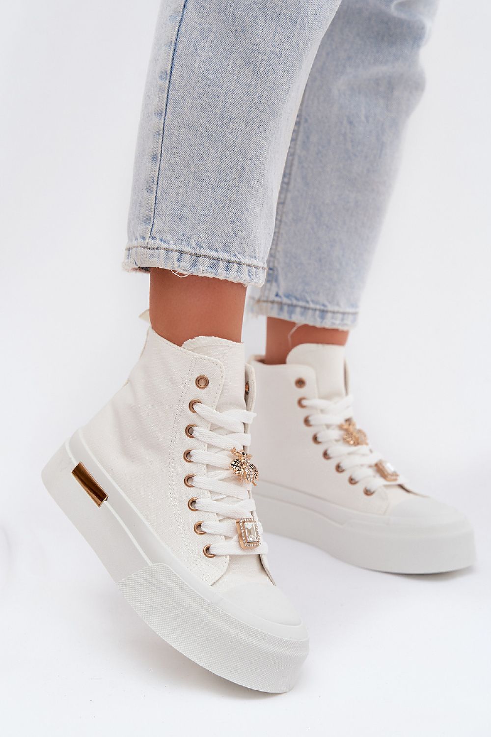 White high-top sneakers with gold accents worn with light blue jeans on a white background