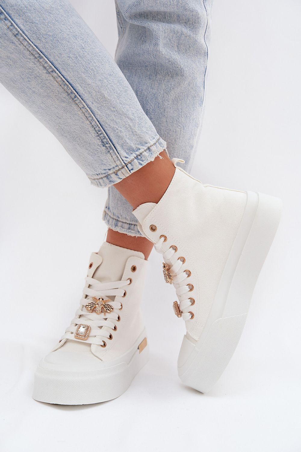 White sneakers with gold accents worn with light blue jeans on a white background