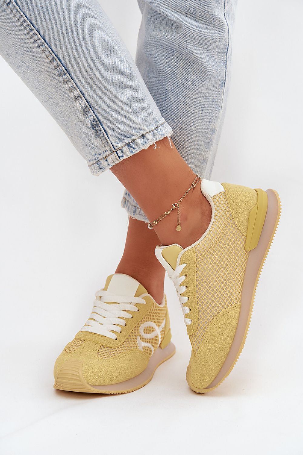 Yellow sneakers worn with light blue jeans on a white background