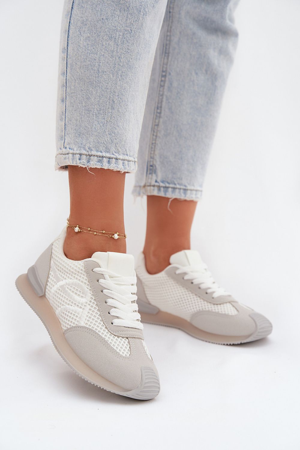White sneakers with gray soles worn with light blue jeans on a white background