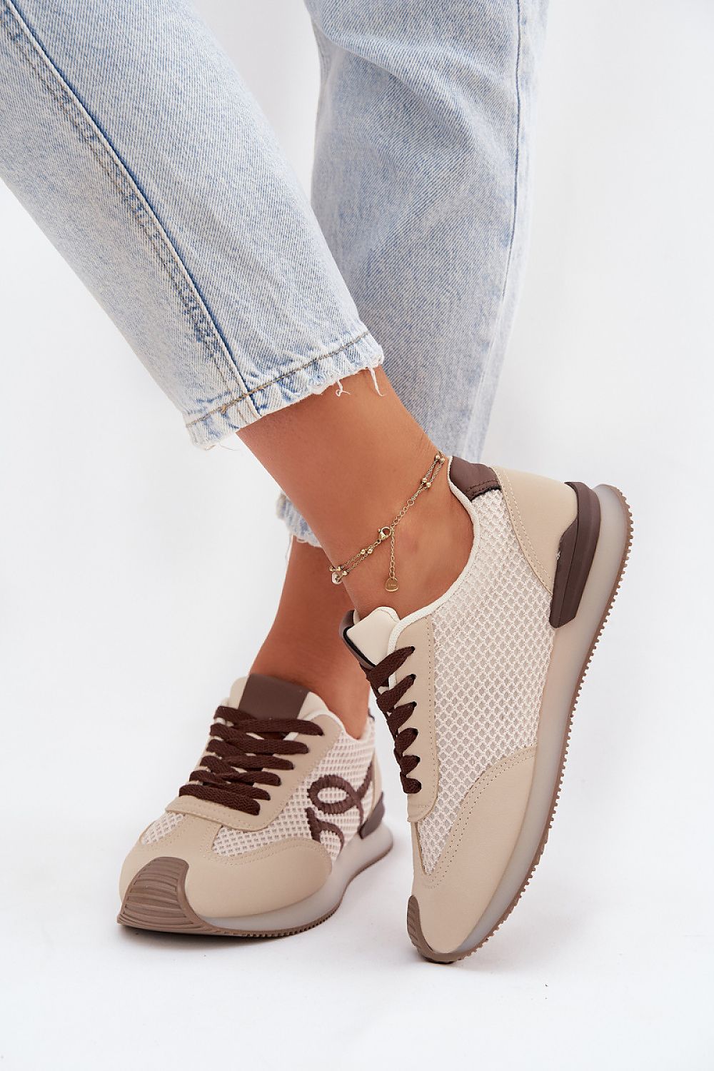 Beige and brown sneakers worn with light blue jeans on a white background
