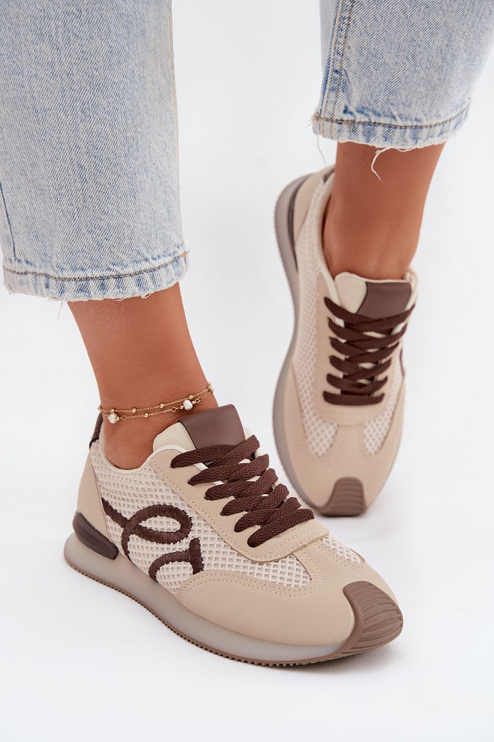 Beige and brown sneakers worn with light blue jeans on a white background