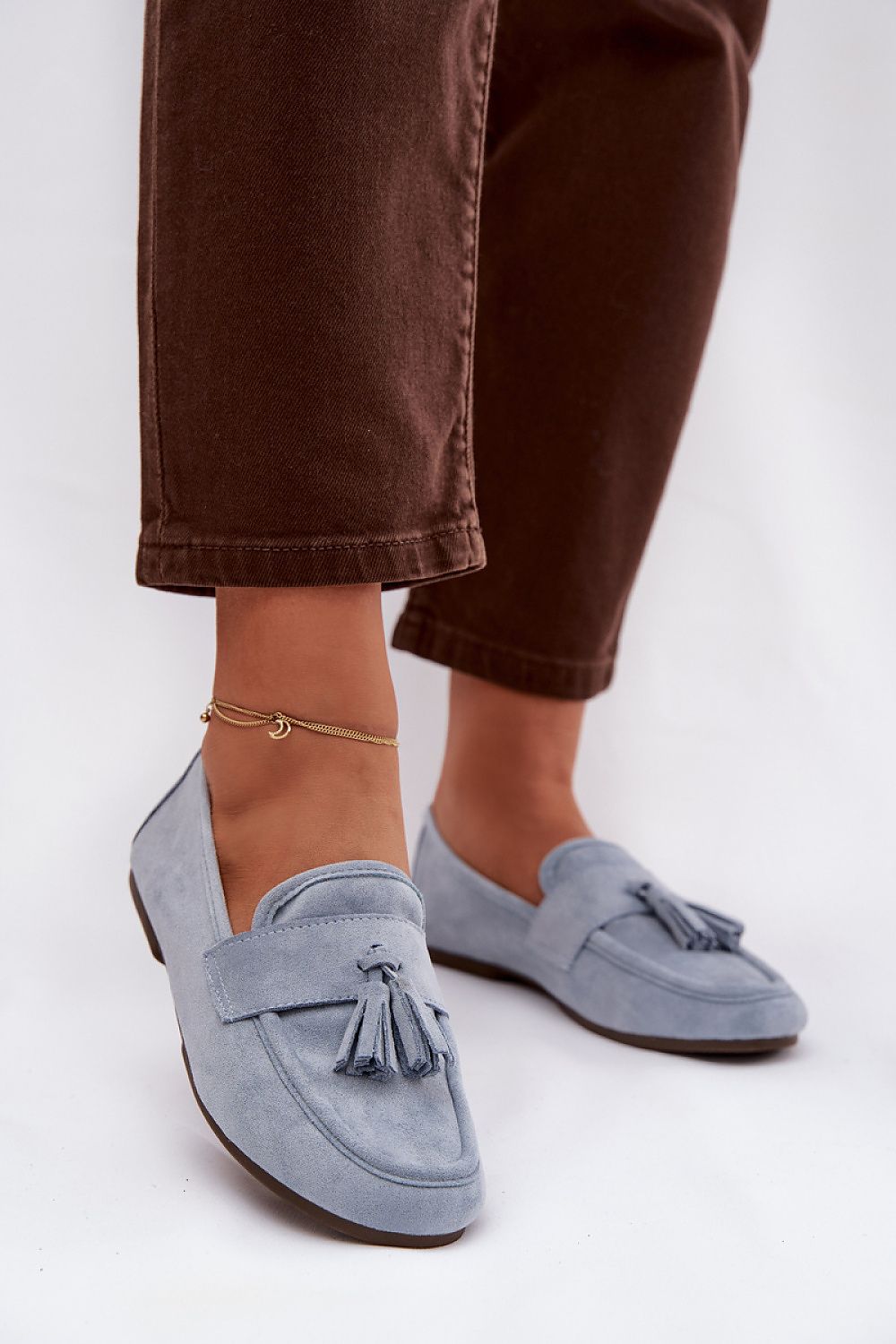Blue loafers with tassels worn with brown pants on a white background