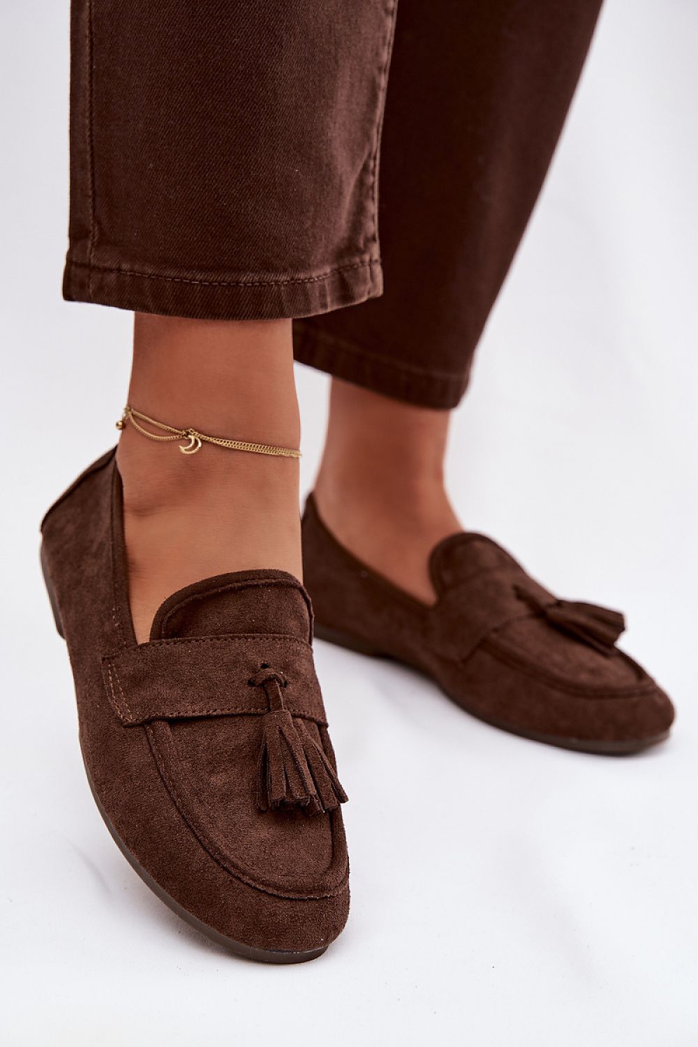 Brown loafers with tassels worn with brown pants on a white background