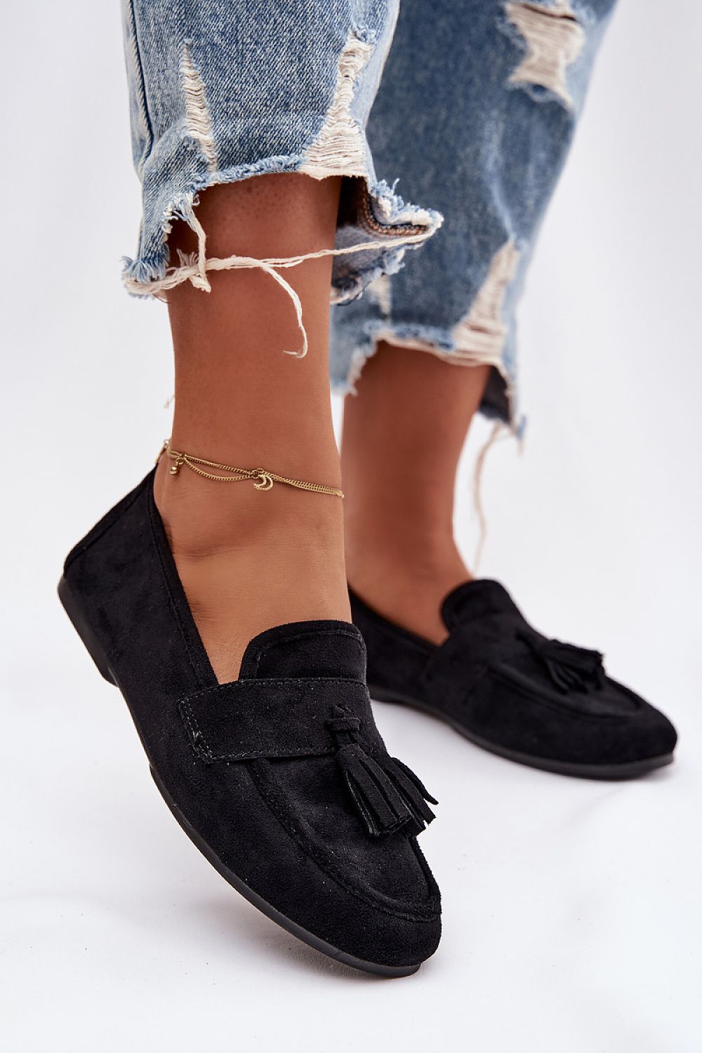 Black loafers with tassels worn with ripped jeans on a white background