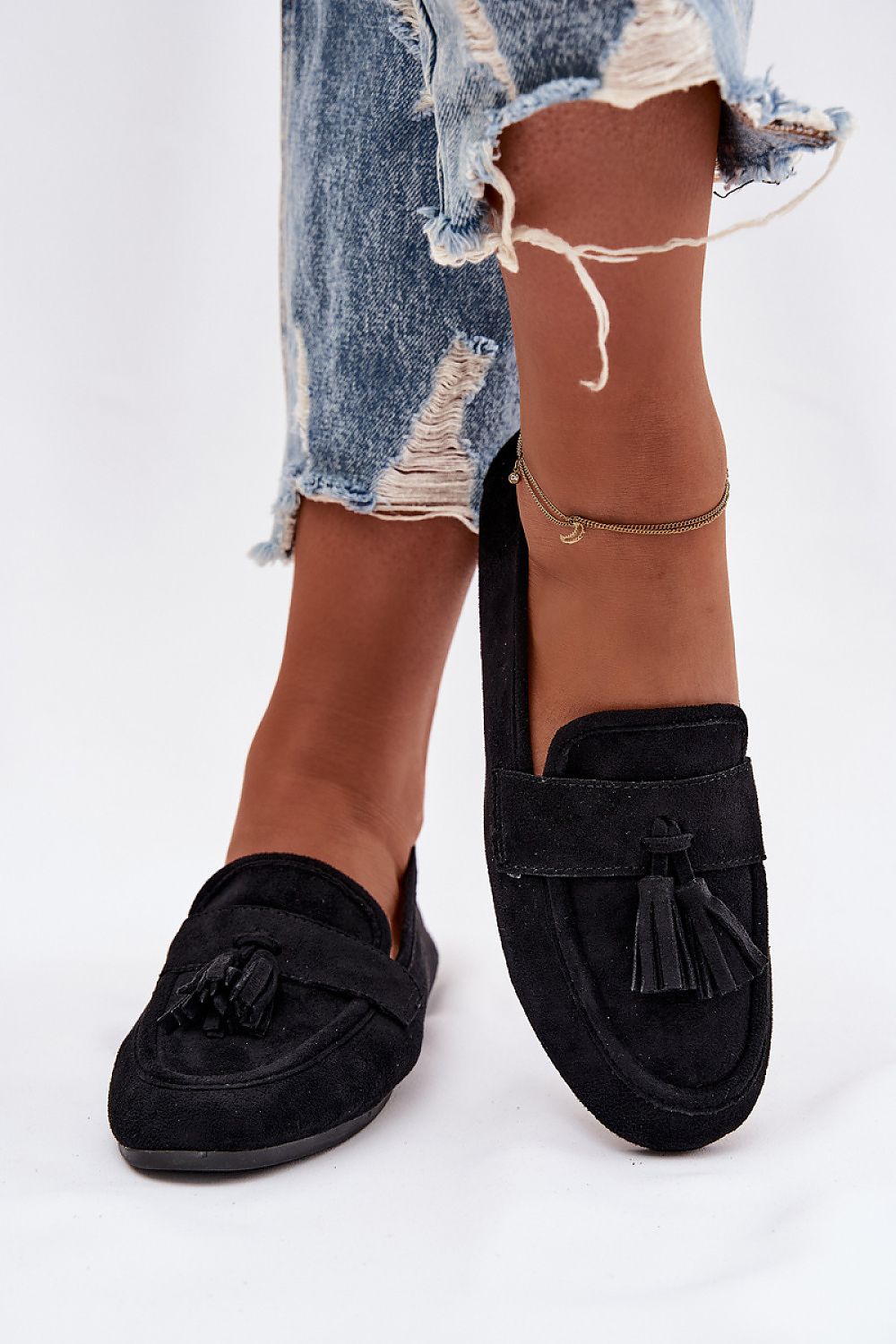 Black loafers worn with ripped jeans on a white background