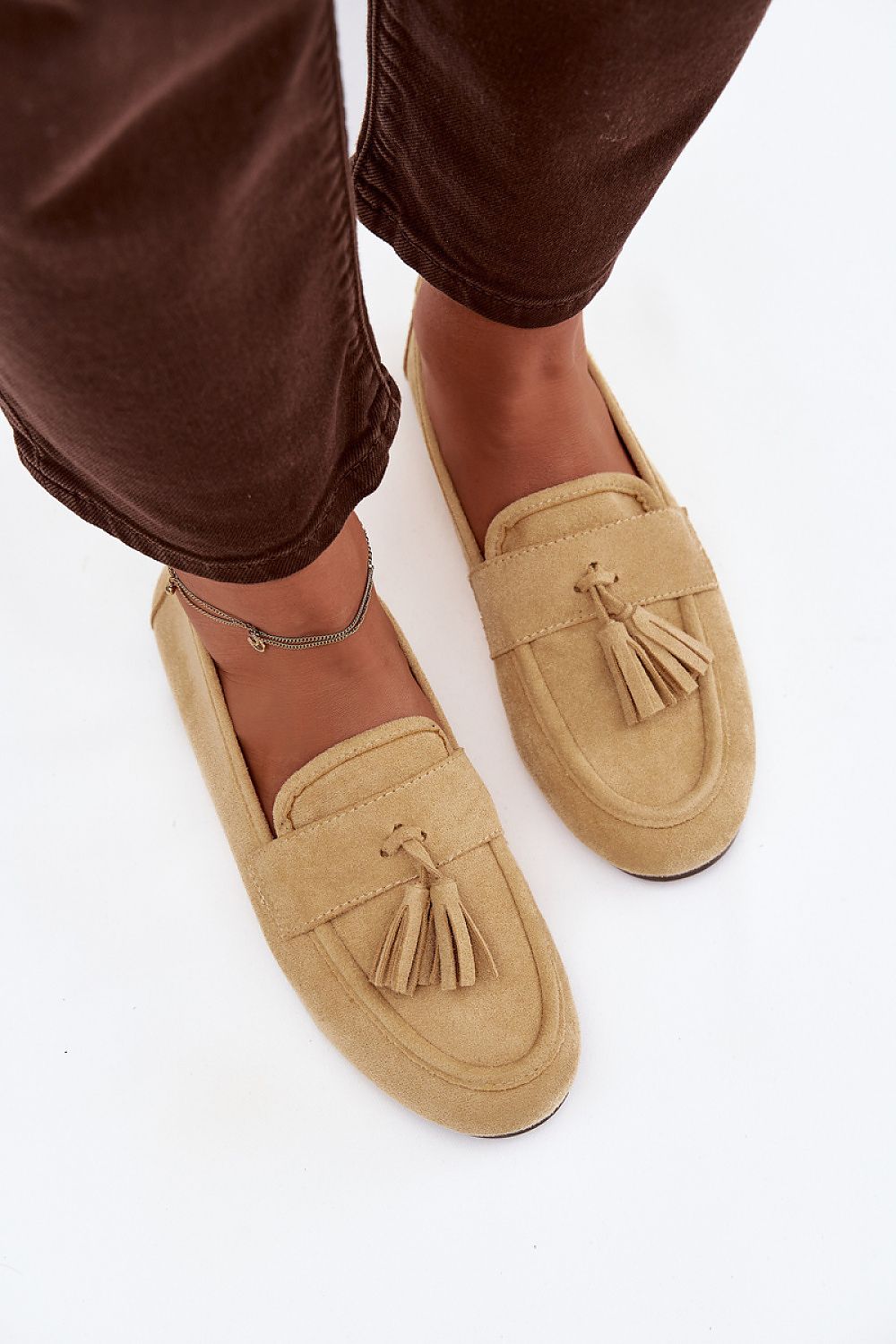 Tan loafers with tassels worn with brown pants on a white background