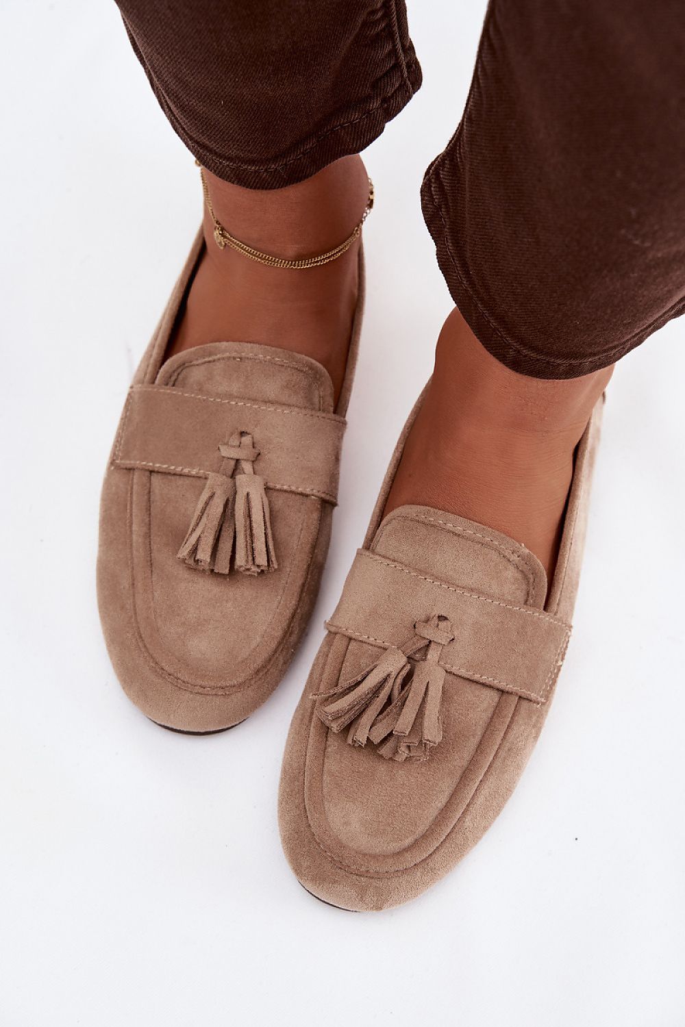 Beige loafers with tassels worn by a person on a white background