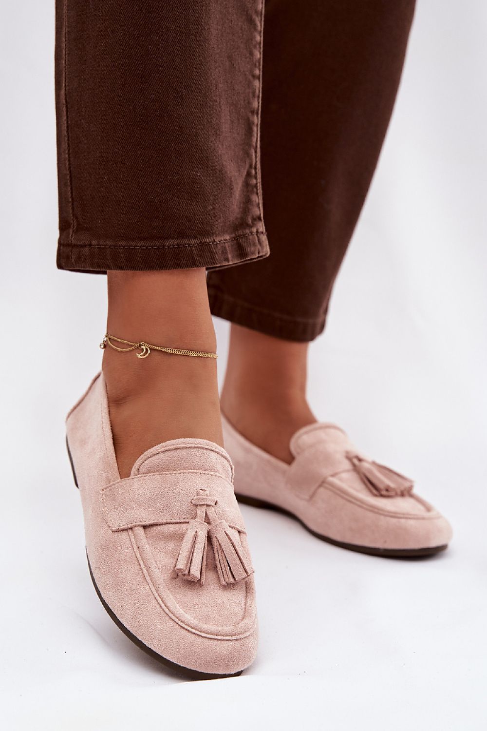 Pink loafers with tassels worn with brown pants on a white background