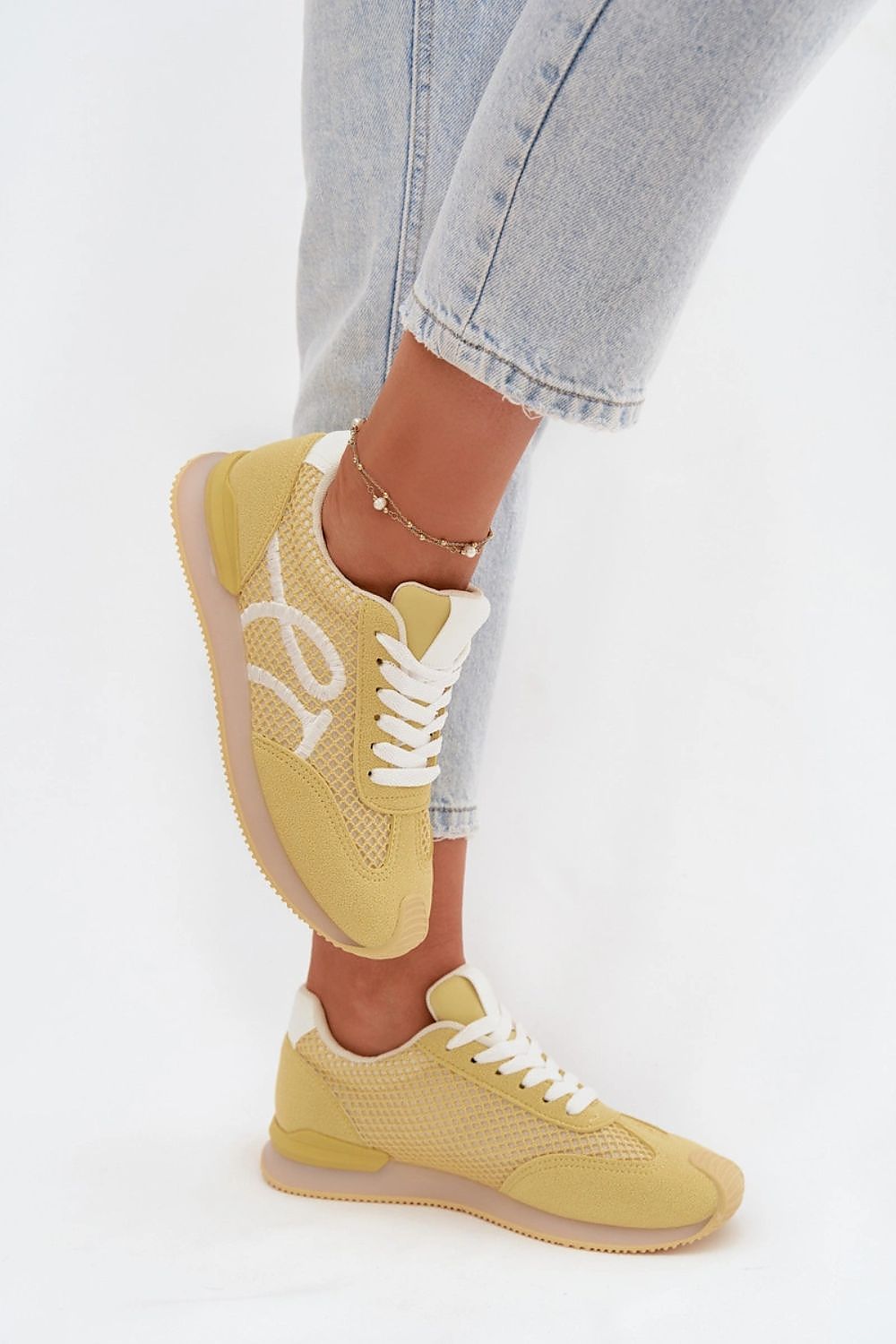 Yellow sneakers worn with light blue jeans on a white background