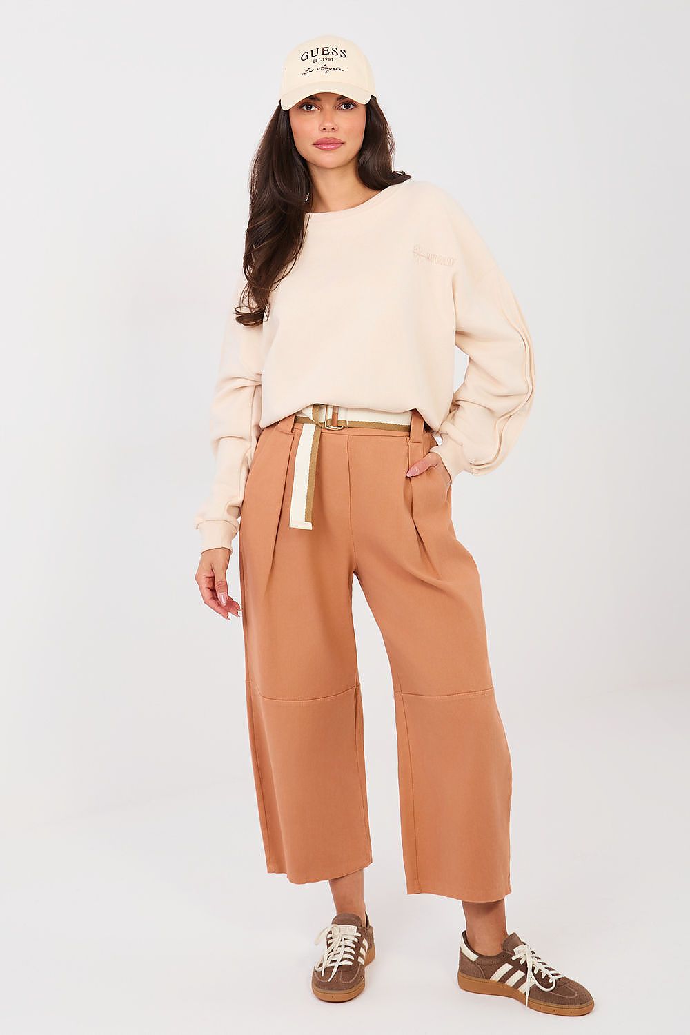 Woman wearing a beige sweater, tan pants, and a cap on a white background