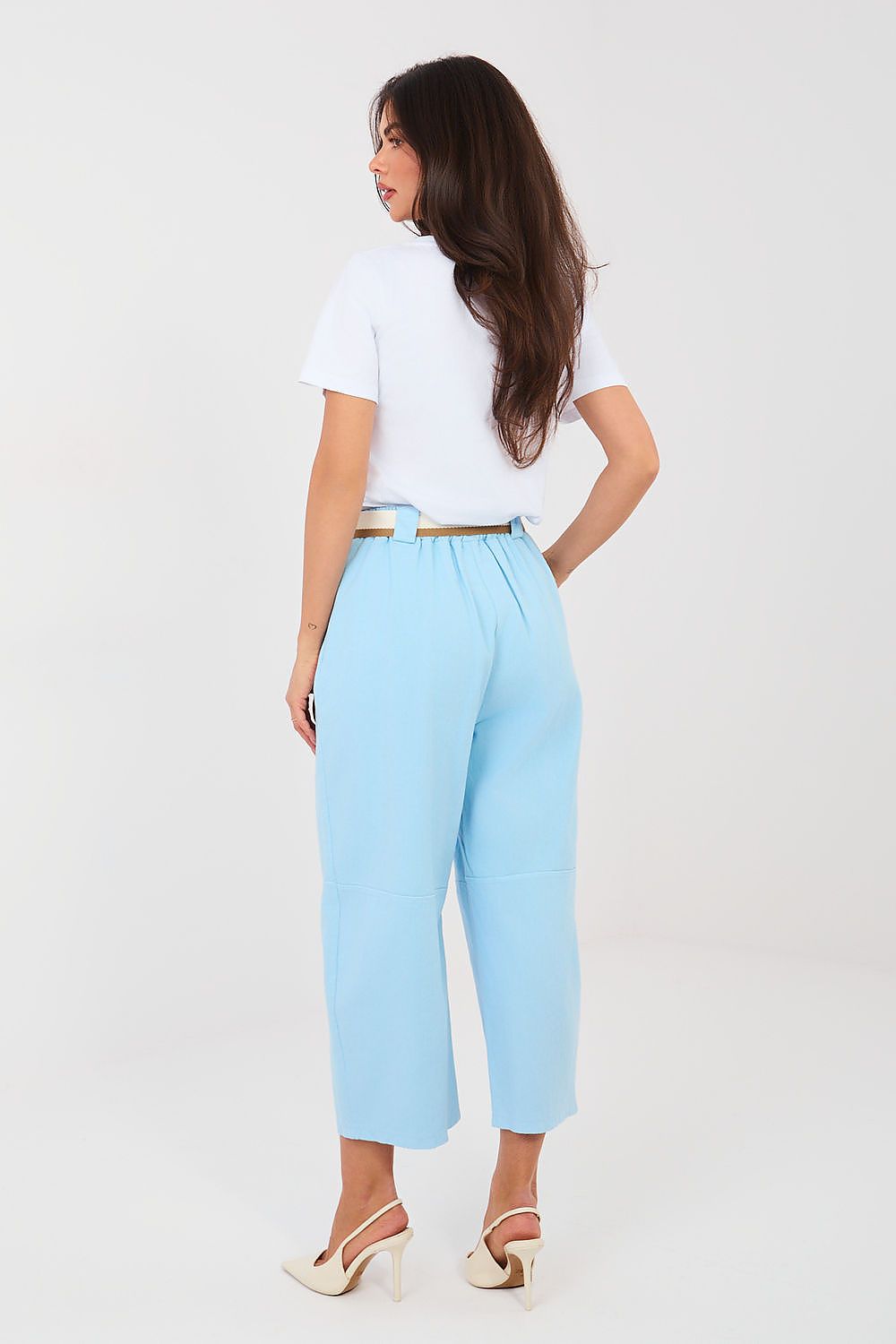 Woman wearing light blue pants and a white top on a plain background