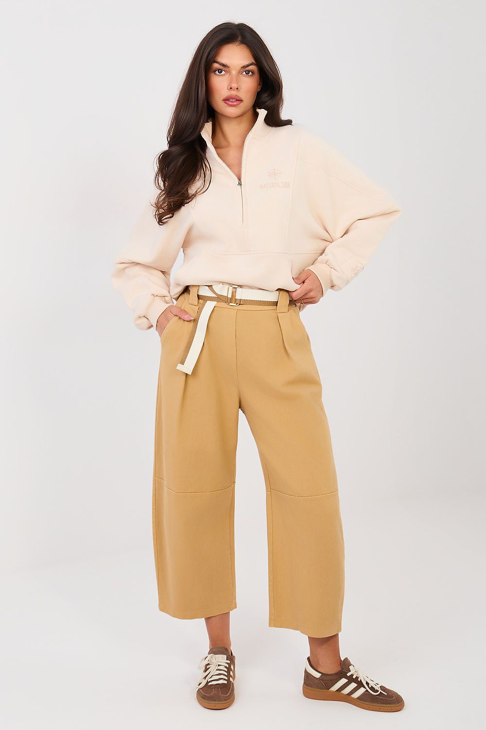 Woman wearing a cream jacket and mustard yellow pants on a white background