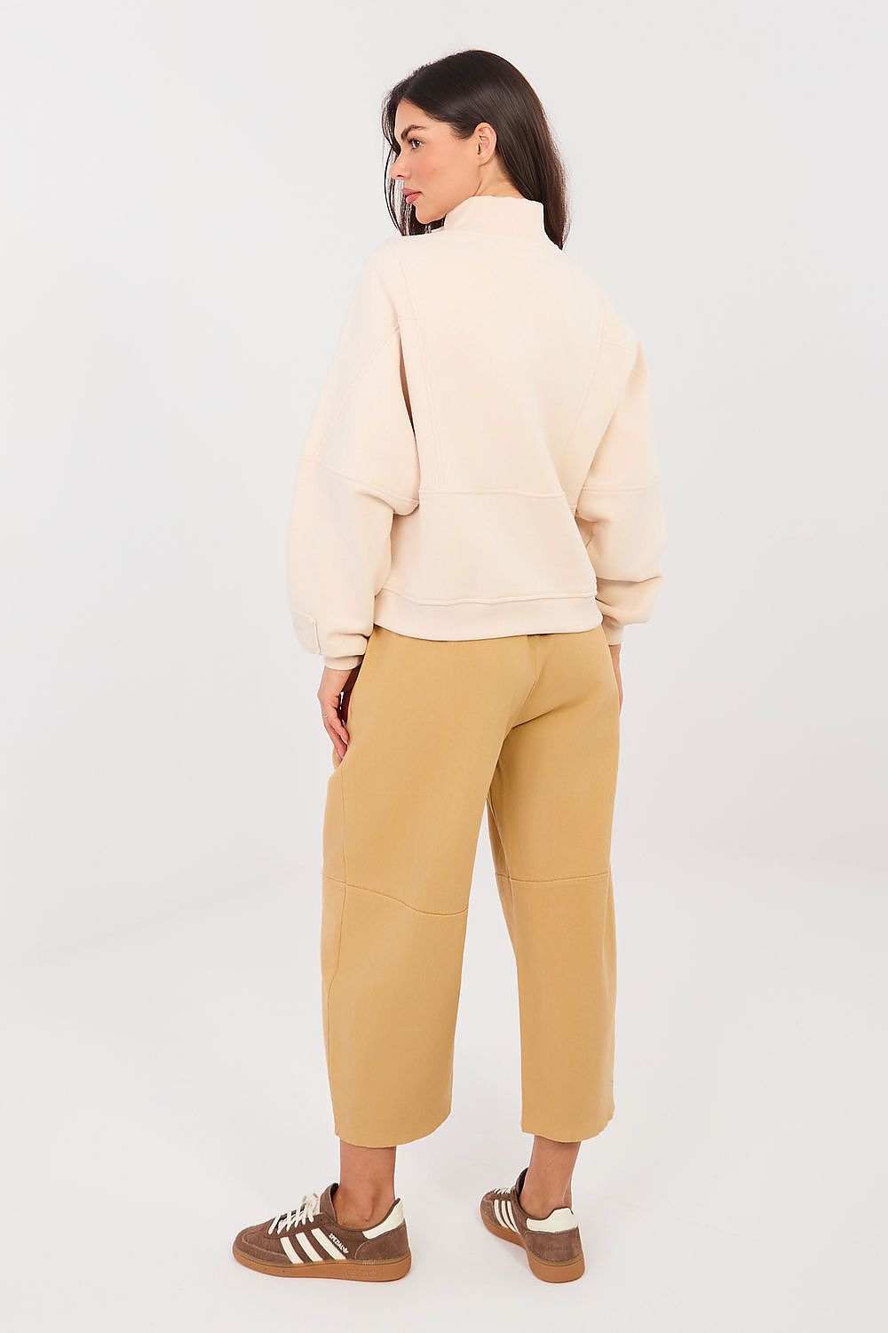 Woman wearing a cream sweater and beige pants on a white background