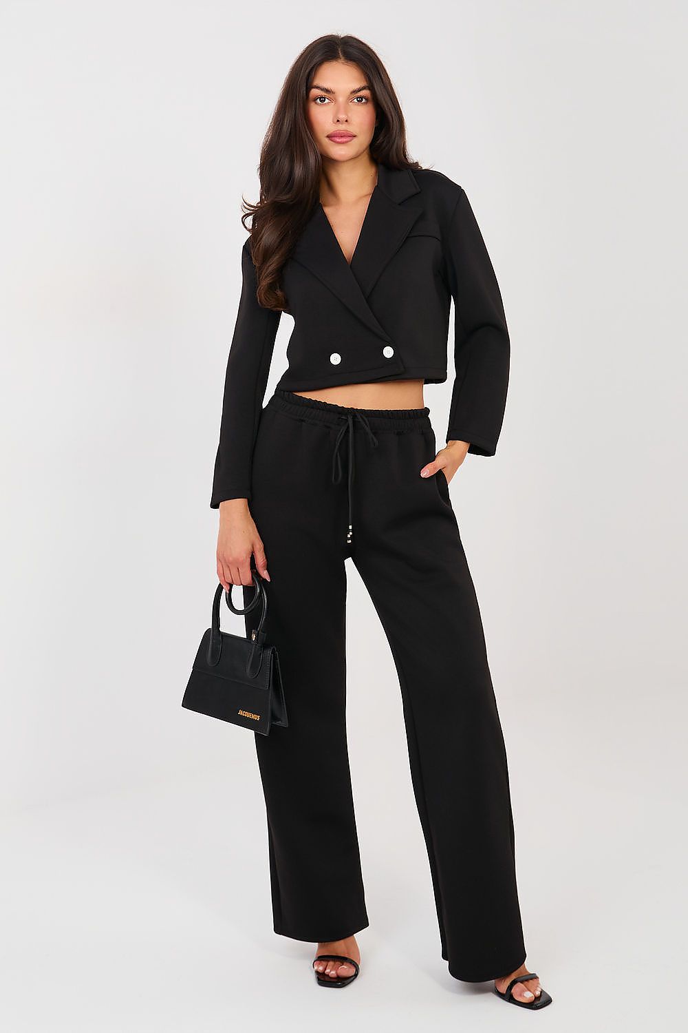 Woman wearing a black outfit with a cropped blazer and wide-leg pants on a white background