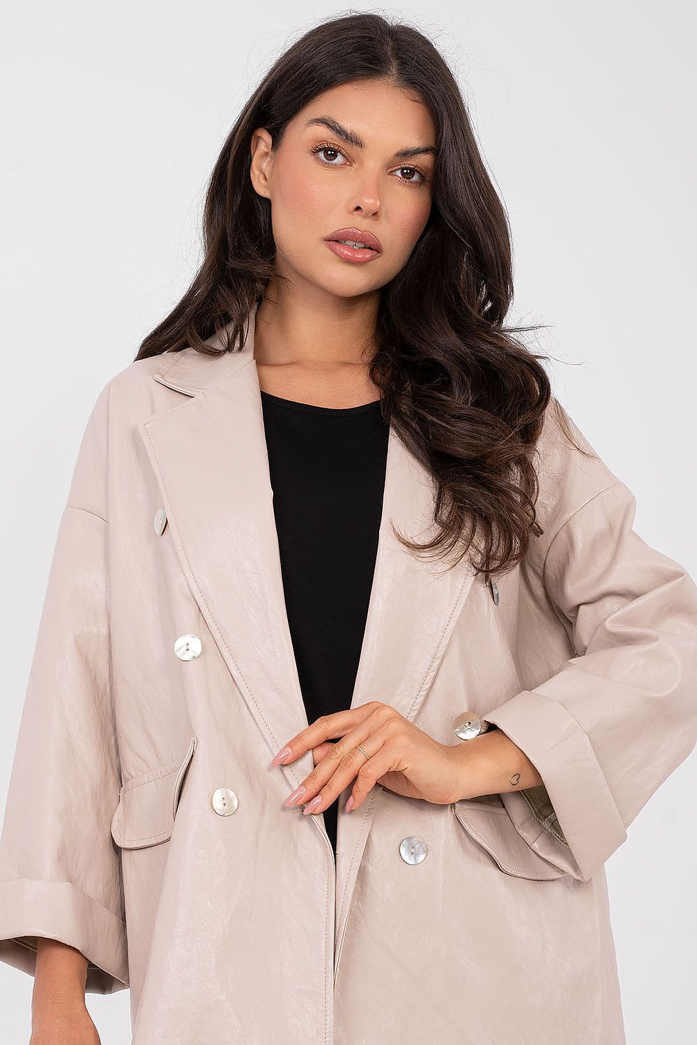 Woman wearing a beige coat over a black top on a plain background