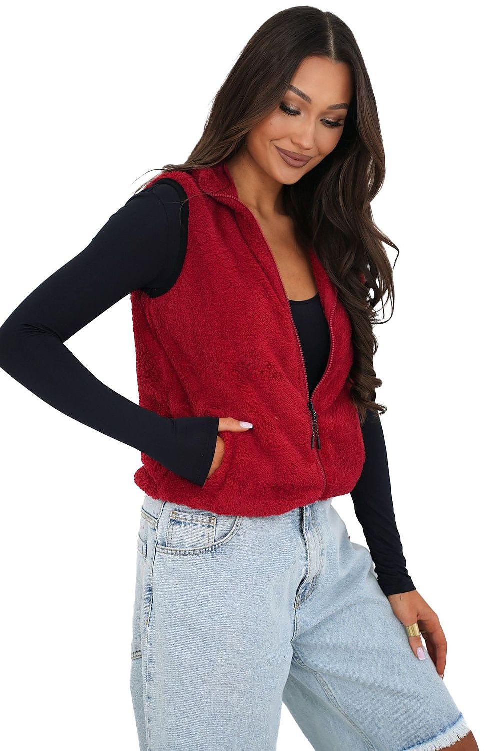 Woman wearing a red vest over a black long-sleeve shirt and light blue jeans on a white background