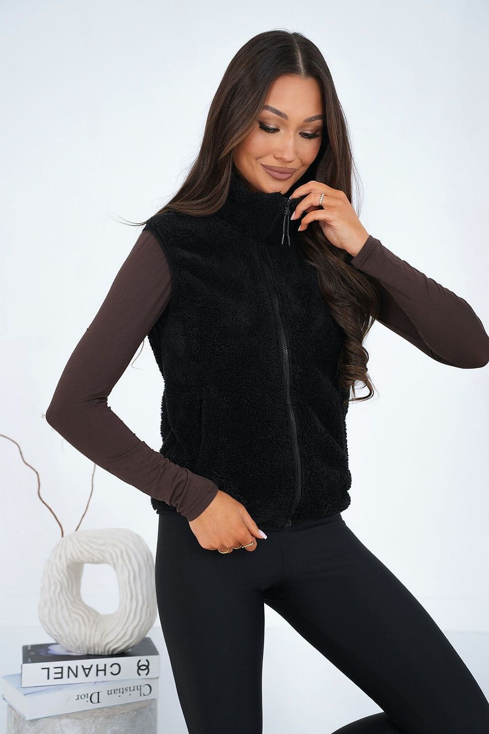 Woman wearing a black vest over a brown long-sleeve top with a white background
