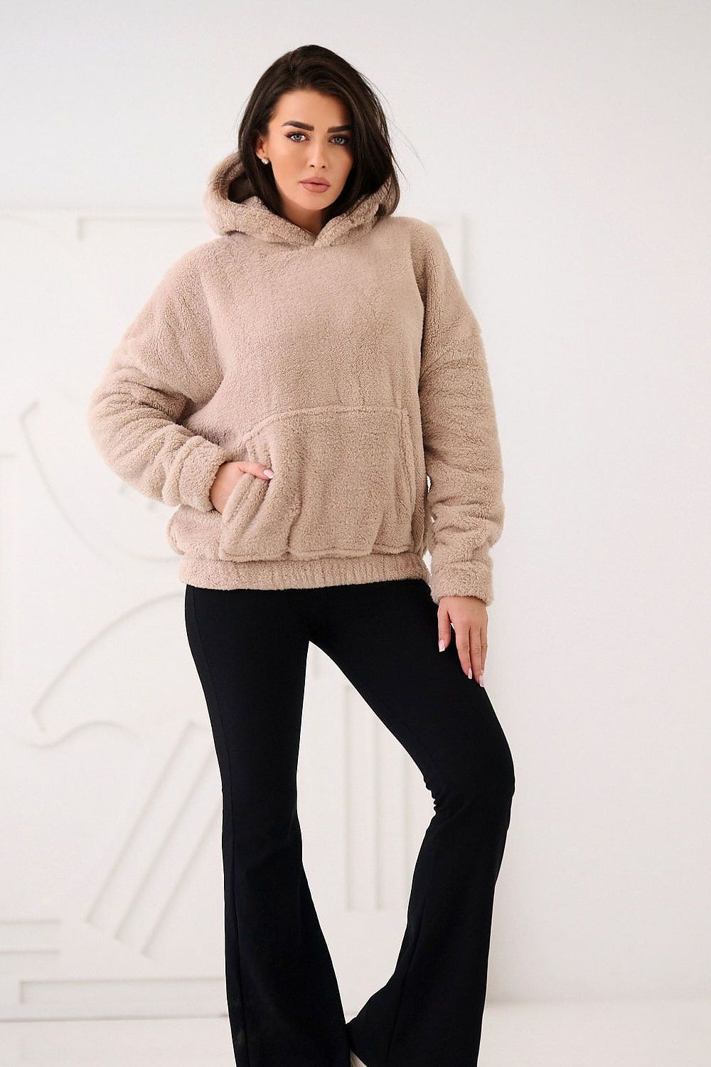Woman wearing a beige hoodie and black pants against a white background