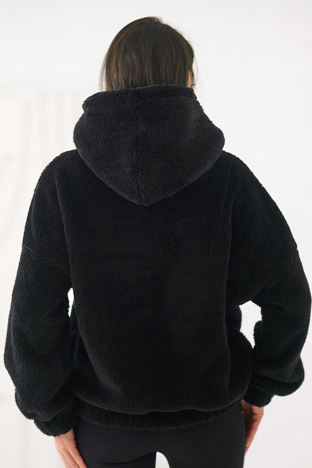 Person wearing a black fleece jacket with a hood on a white background