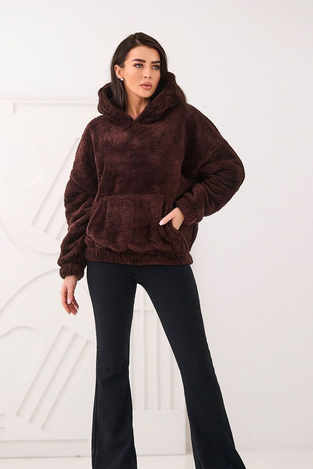 Woman wearing a brown fleece hoodie and black pants on a white background