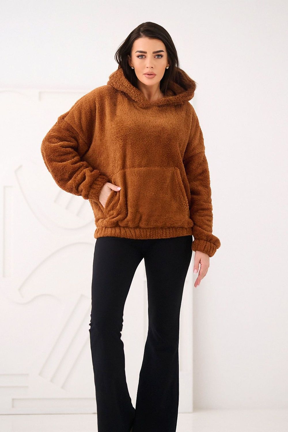Woman wearing a brown fleece hoodie and black pants on a white background