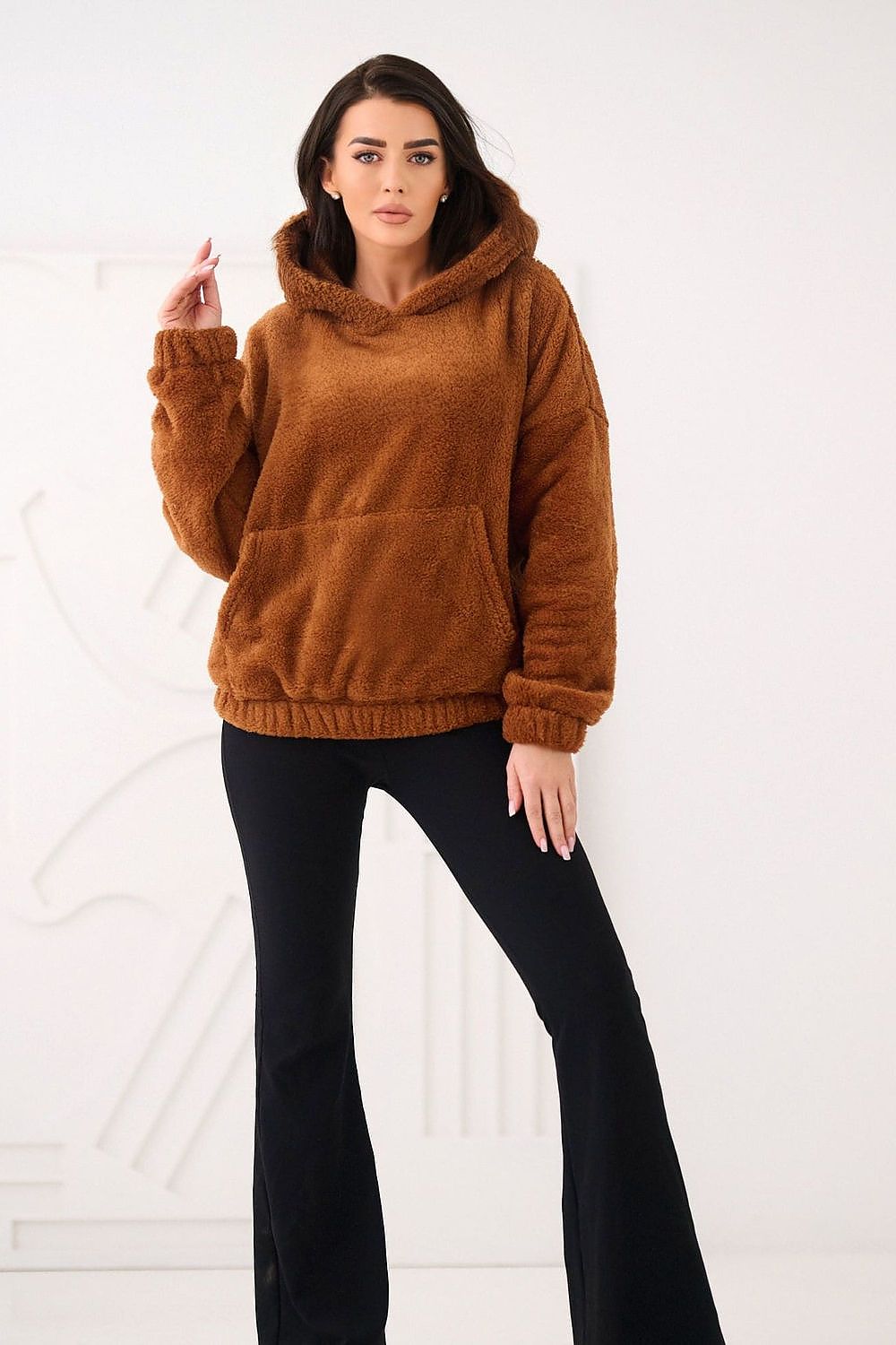 Woman wearing a brown fleece hoodie and black pants on a white background