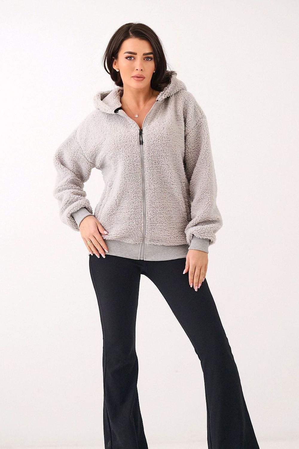 Woman wearing a gray zip-up hoodie and black pants on a white background
