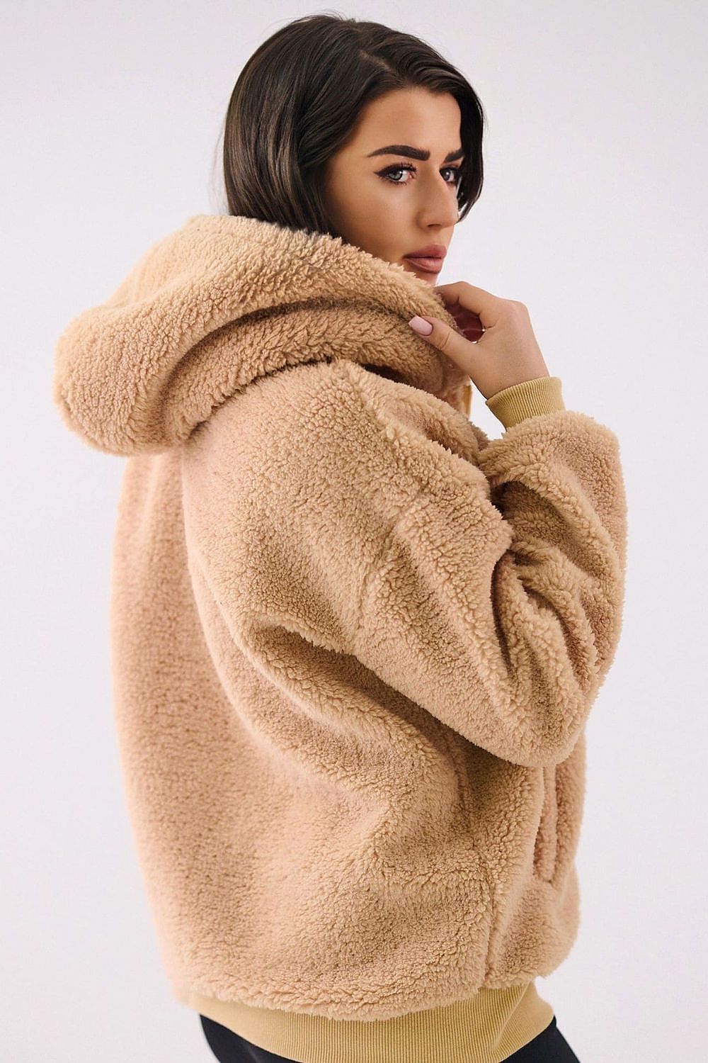 Woman wearing a beige sherpa jacket against a white background