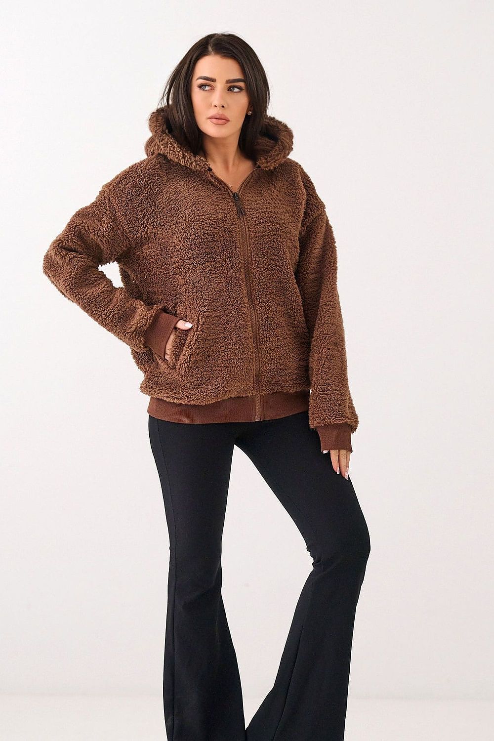 Woman wearing a brown fleece hoodie and black pants on a white background