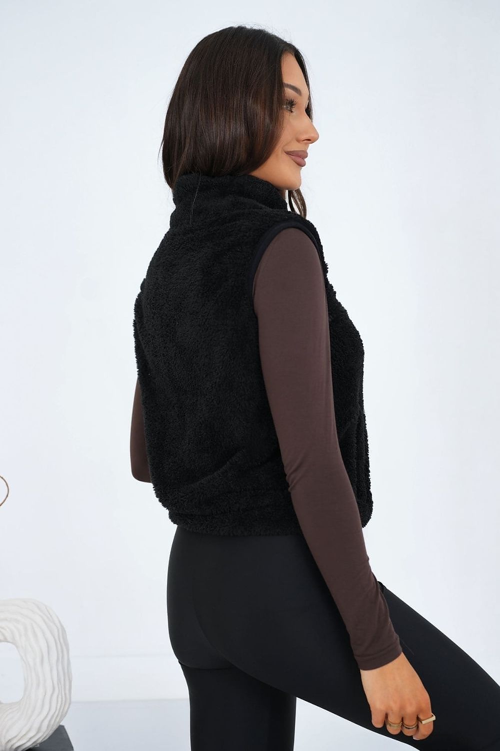 Woman wearing a black puffer vest over a long-sleeve shirt on a white background