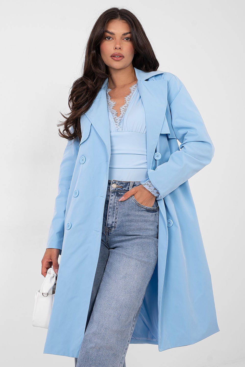 Woman wearing a light blue coat over a white top and jeans on a white background