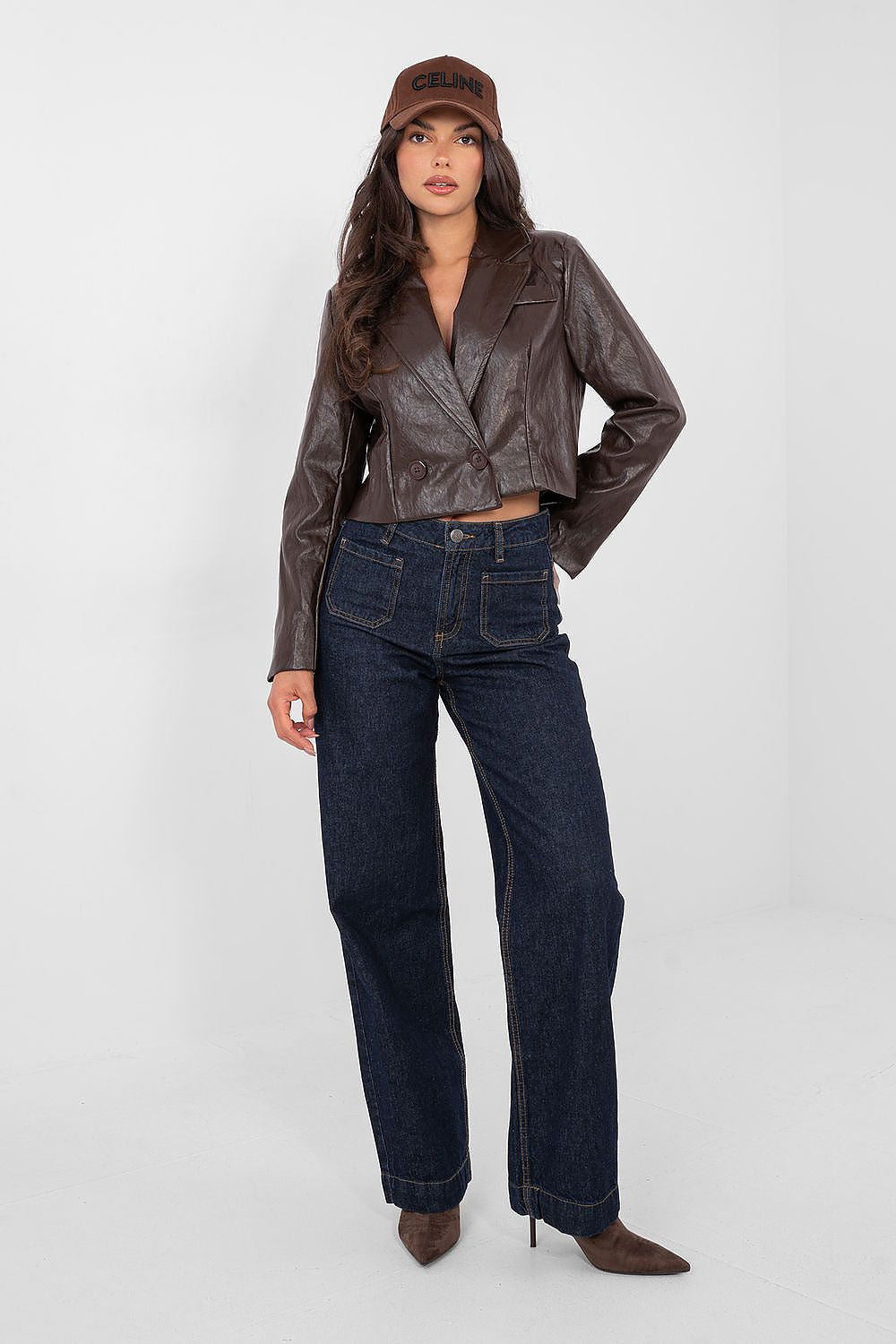 Woman wearing a brown leather jacket and dark jeans on a white background