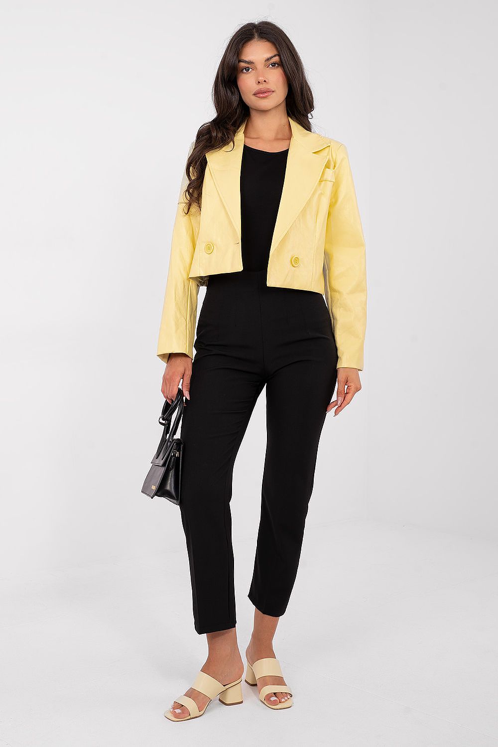 Woman wearing a yellow jacket, black top, and pants on a white background
