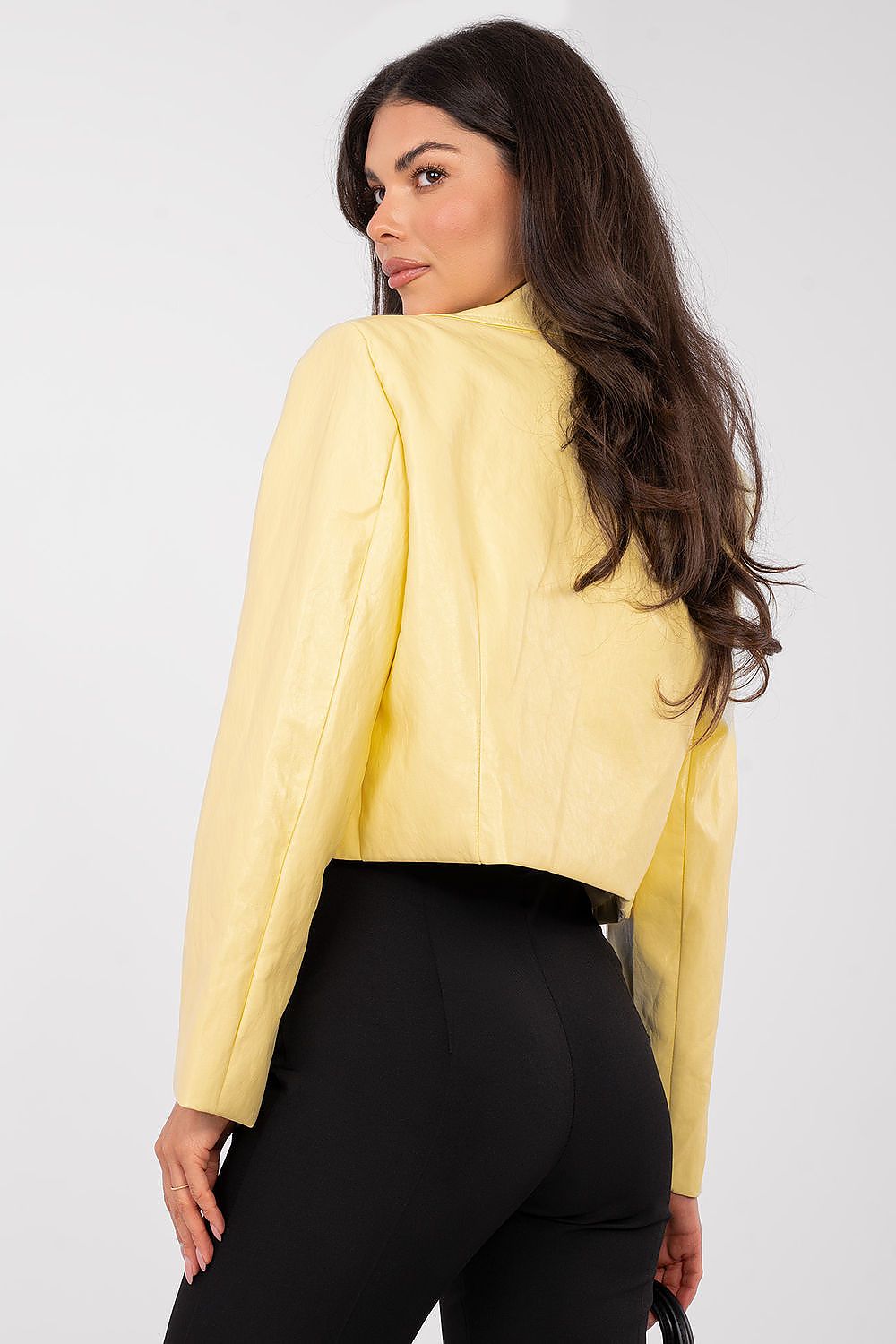 Woman wearing a yellow blazer and black pants against a white background
