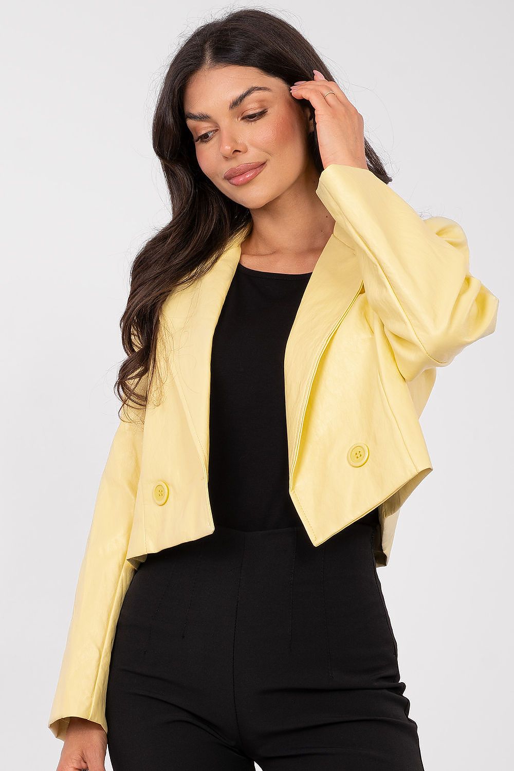 Woman wearing a yellow blazer over a black outfit on a light gray background