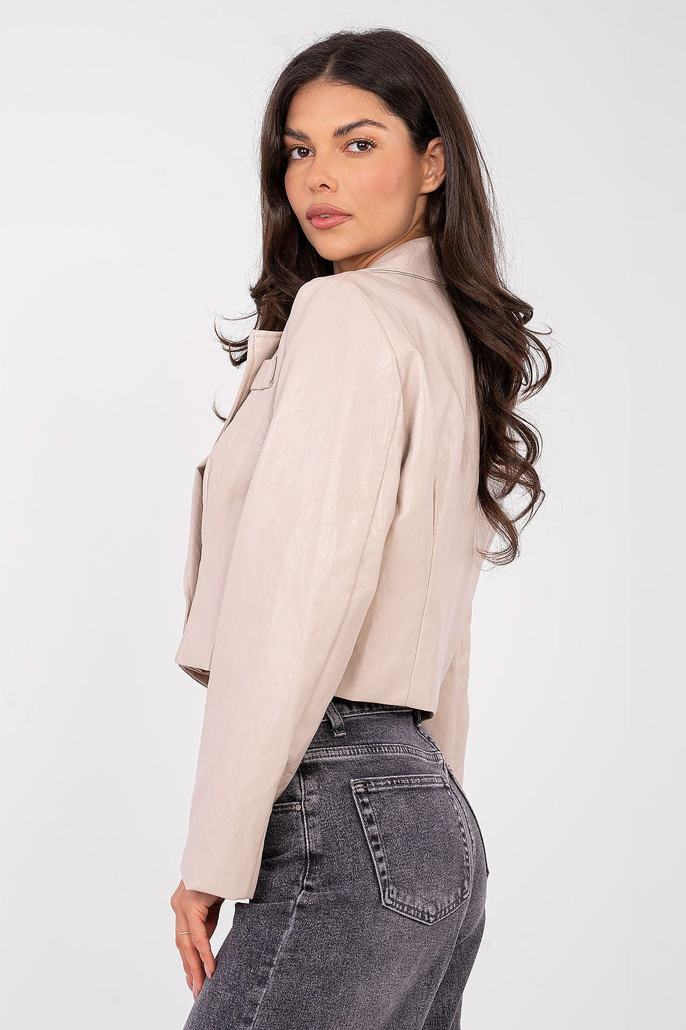 Woman wearing a beige blazer and gray jeans on a white background