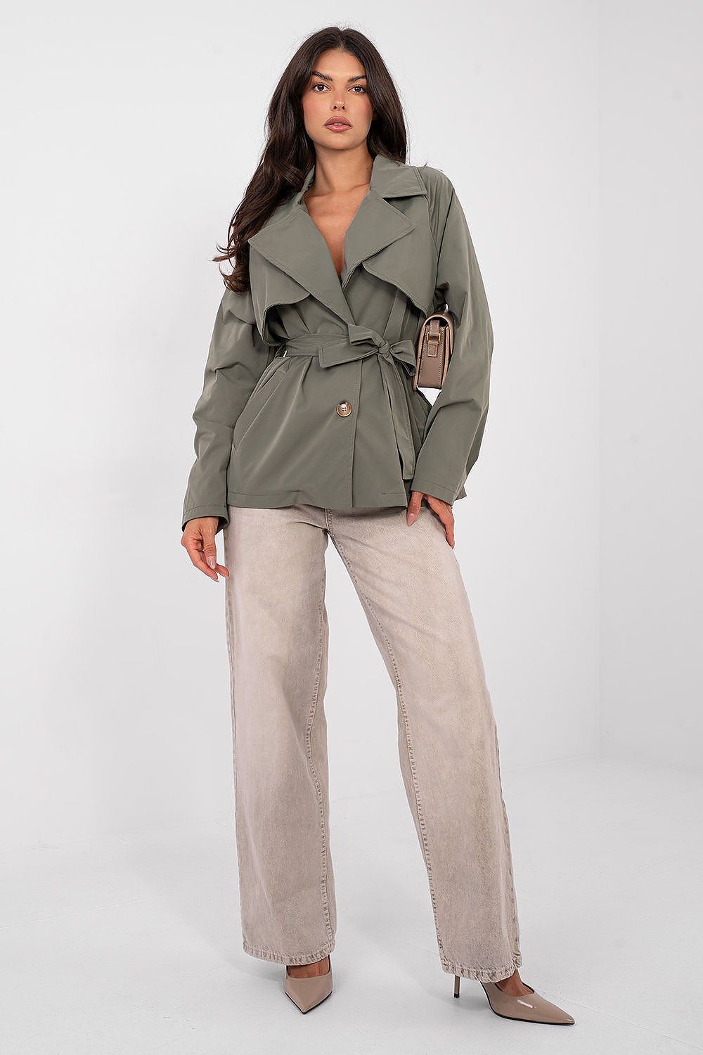 Woman wearing a green trench coat and beige pants on a white background