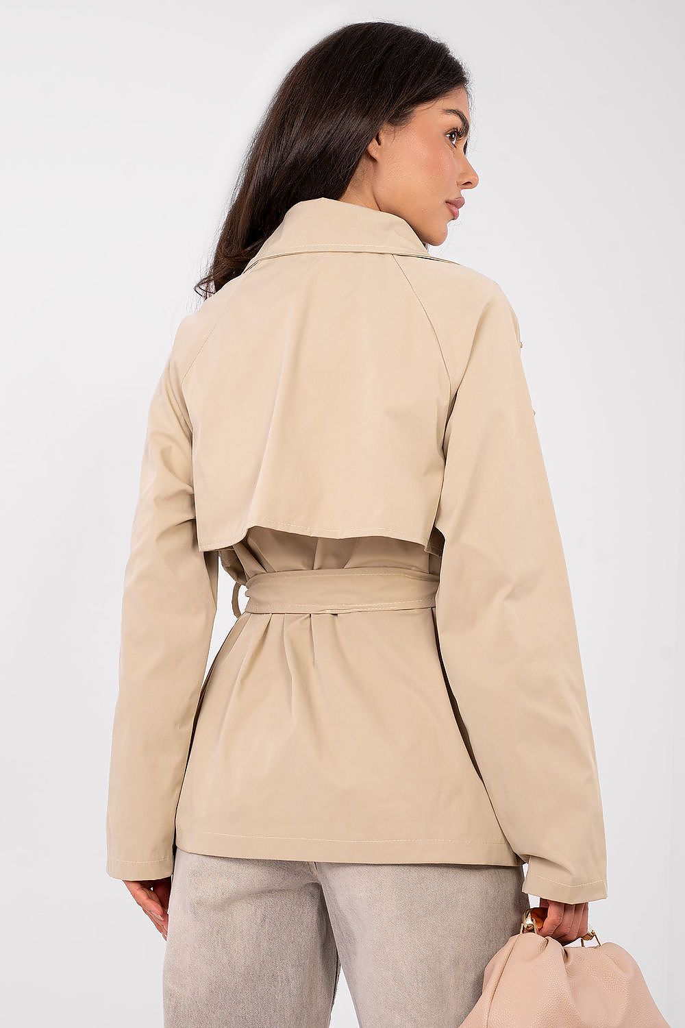 Woman wearing a beige trench coat against a white background