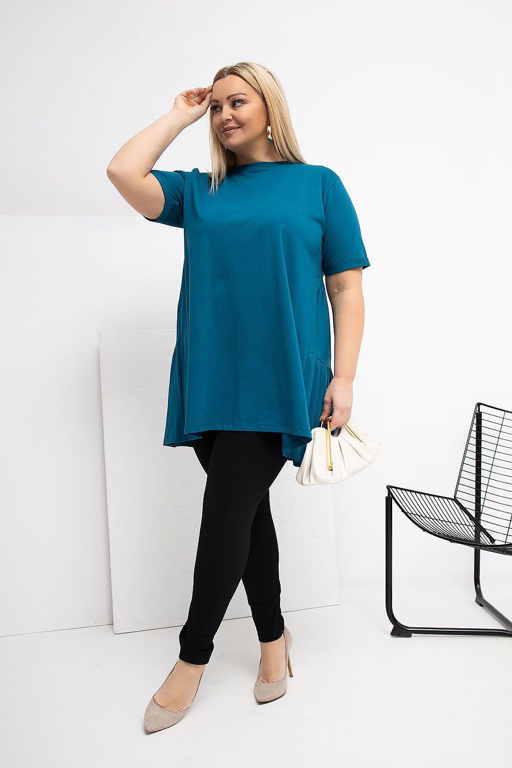 Woman wearing a teal dress and black leggings against a white background