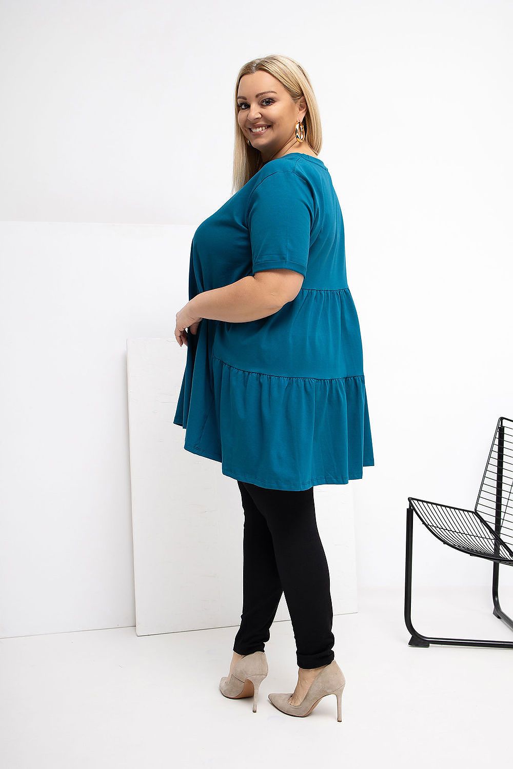 Woman wearing a teal dress with black leggings against a white background