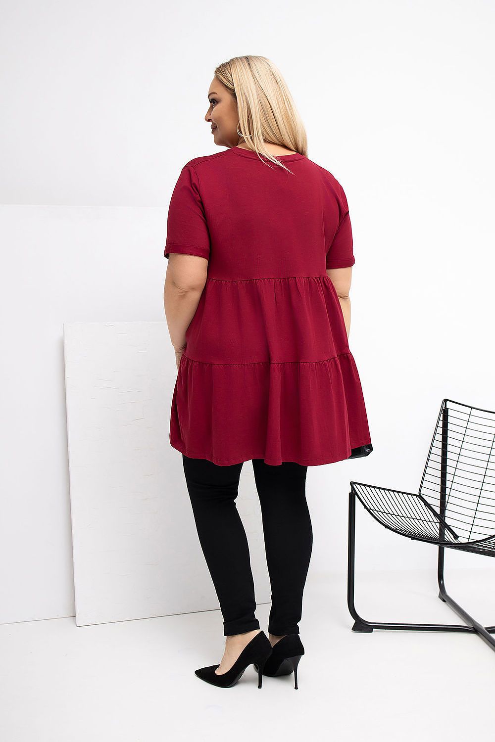 Woman wearing a red dress with black pants and high heels, standing against a white background.