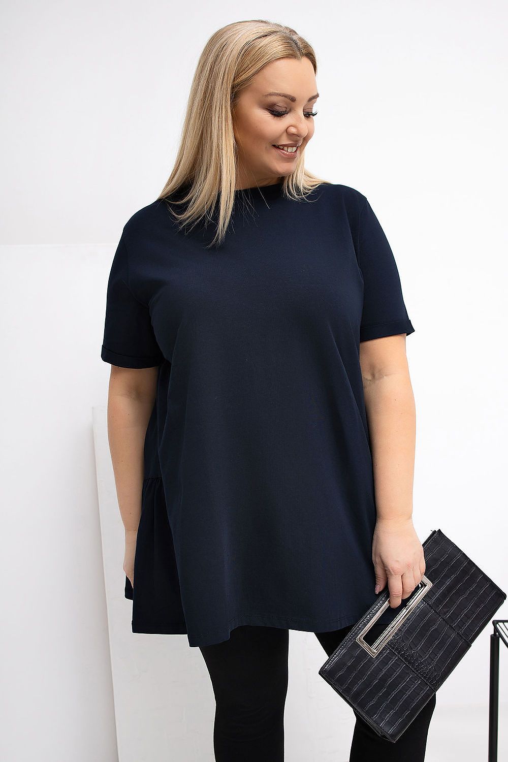 Woman wearing a navy blue t-shirt and holding a black clutch against a white background